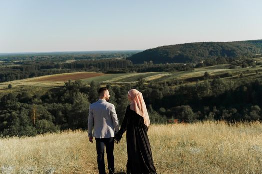 Muslim love story. Mixed couple smiles and hugs on the green hills . Woman weared in hijab looks to her man. Advert for on-line dating agency