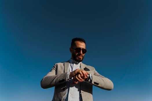 Handsome bearded arabian man in sunglasses on the blue sky background. Confident muslim business man. Arab man weared in grey coat