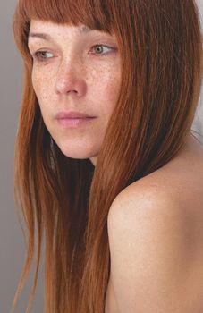 Portrait of caucasian middle-aged woman with reddish hair and freckles looking aside over gray background