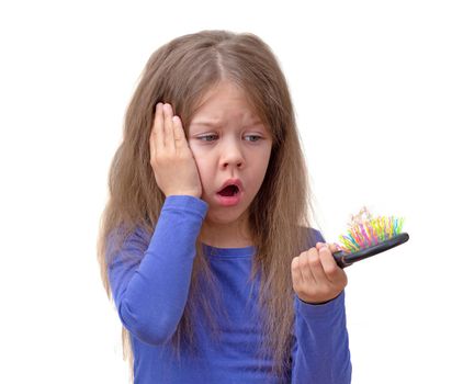 Isolated scared and shocked caucasian little girl of 5-6 years with long hair, looking at hair brush with piece of hair on it on white background in blue