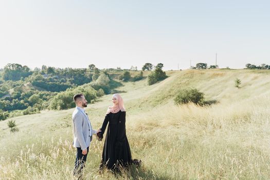 Muslim love story of mixed couple. Man and woman smiles and walks on the green hills . Woman weared in hijab looks to her man. Advert for on-line dating agency