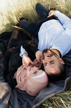 Muslim love story. Mixed couple lays on the grass, smiles and hugs.. Woman weared in hijab looks to her man. Advert for on-line dating agency