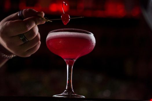 Classic Pink Lady cocktail closeup with flower and cherry on bar counter