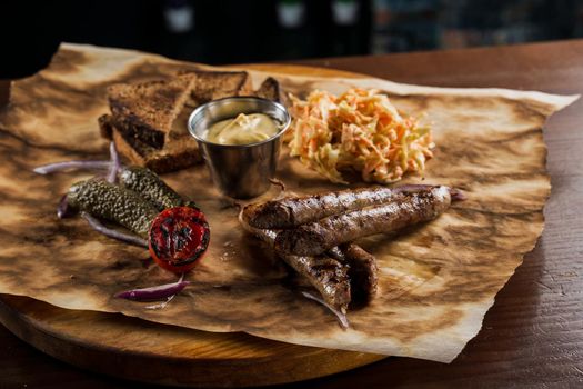 Grilled sausages with beer and vegetables with pickled cucumber, cabbage salad sauce and bread on parchment, top view.