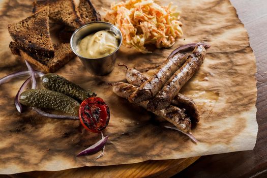 Grilled sausages with beer and vegetables with pickled cucumber, cabbage salad sauce and bread on parchment, top view.