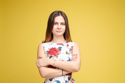 Studio portrait of fashionable brunette lady in white dress with flowers and beige heels posing with bent leg. Smiling at camera. holding skirt. Isolate on yellow background.