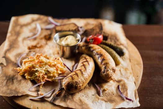 Grilled sausages with beer and vegetables with pickled cucumber, cabbage salad sauce and bread on parchment, top view.