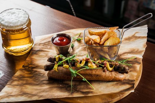 Barbecue grilled hot dog and beer with yellow mustard and ketchup on wooden background. Hot dog sandwich with potato fries and sauces.