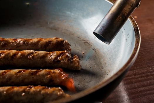Grilled sausages in a frying pan are fired with a gas burner