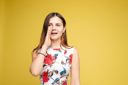 Studio portrait of curious brunette girl in multicolored top listening to the news or gossips with her ear.