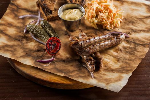 Grilled sausages with beer and vegetables with pickled cucumber, cabbage salad sauce and bread on parchment, top view.