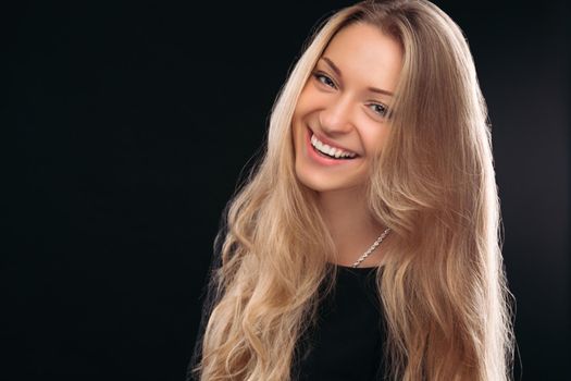 Studio portrait of happy beautiful girl with posing in studio on black background and smiling at camera. Beautiful model wearing black with perfect makeup after salon. Concept of beauty.