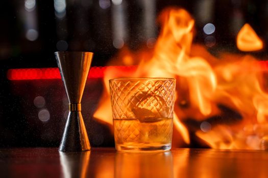 The bartender makes flame over a cocktail with orange peel close up.