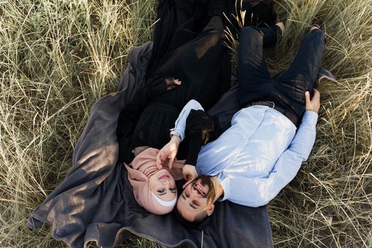 Muslim love story. Mixed couple lays on the grass, smiles and hugs.. Woman weared in hijab looks to her man. Advert for on-line dating agency