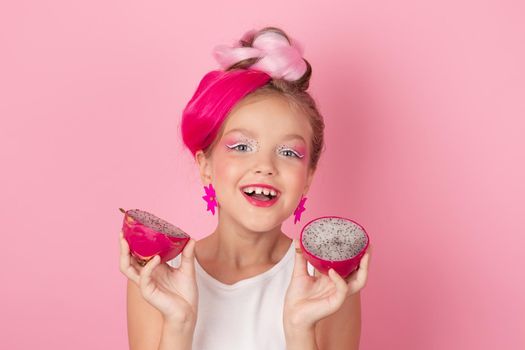 Close-up portrait of pretty girl with pink hairstyle with dragon fruit on pink background. Studio shot of charming tween girl with pink make up enjoying juicy red pitaya. exotic Pitahaya fruit.