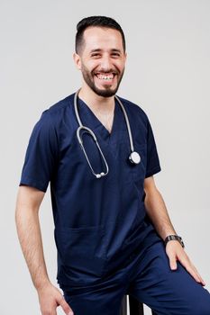 Arabian medical student with stethoscope in surgical uniform smiles on blanked background. Handsome bearded arab man in studio. Confident doctor at consultation