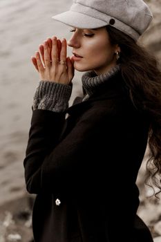 A beautiful girl close-up in a black coat and a gray woolen cap near the lake. Traveling in your country