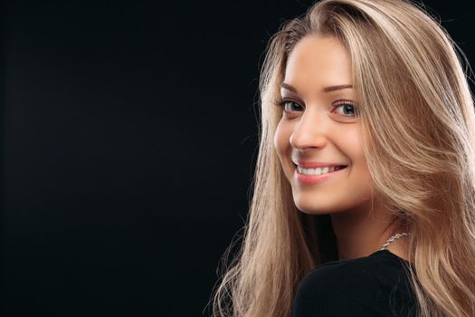 Studio portrait of happy beautiful girl with posing in studio on black background and smiling at camera. Beautiful model wearing black with perfect makeup after salon. Concept of beauty.