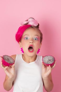 Close-up portrait of pretty girl with pink hairstyle with dragon fruit on pink background. Studio shot of charming tween girl with pink make up enjoying juicy red pitaya. exotic Pitahaya fruit.