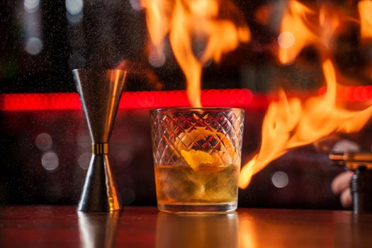 The bartender makes flame over a cocktail with orange peel close up.