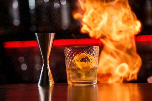 The bartender makes flame over a cocktail with orange peel close up.