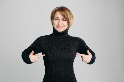Studio portrait of pretty unhappy blonde woman showing by fingers her dirty black sweater. Woman angry because her clothes in pet fur.