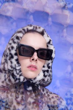 Art portrait, a woman in black glasses and a leopard hoodie on a blue background. High quality photo