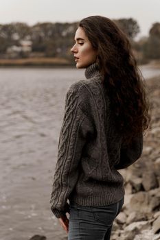 Girl with curly hair on the background of birch with stones and lake in autumn