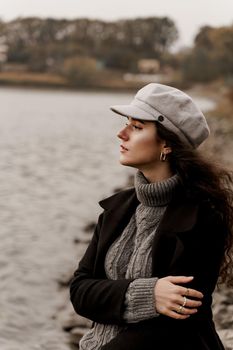 Beautiful girl in a black coat and a gray woolen cap near the lake. Traveling in your country.