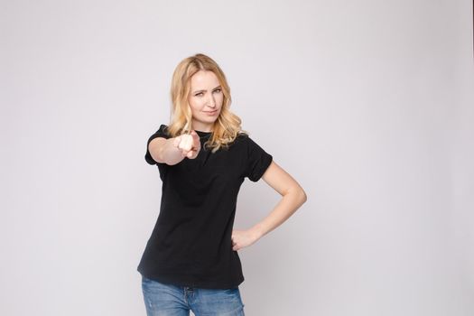 Confident young beautiful woman showing by hand stringent looking at camera posing isolated at white studio background. Accusing female making pointing finger gesture medium long shot