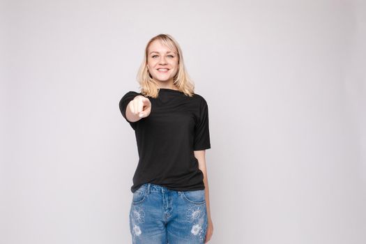 Confident young beautiful woman showing by hand stringent looking at camera posing isolated at white studio background. Accusing female making pointing finger gesture medium long shot