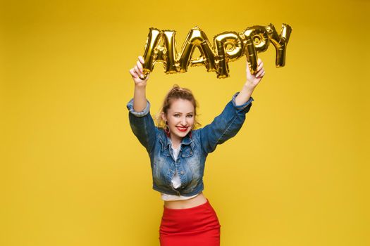 Stock photo portrait of attractive girl with red lips holding shining bright inflatable word HAPPY. Isolate on orange background.