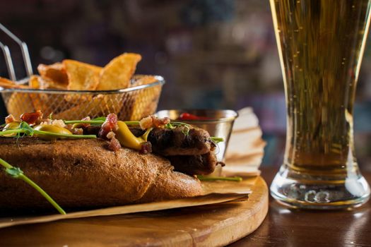 Barbecue grilled hot dog and beer with yellow mustard and ketchup on wooden background. Hot dog sandwich with potato fries and sauces.