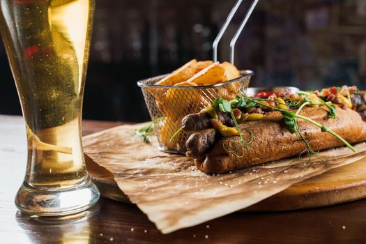 Barbecue grilled hot dog and beer with yellow mustard and ketchup on wooden background. Hot dog sandwich with potato fries and sauces.
