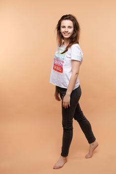 Full length isolate portrait of positive brunette young girl in jeans and t-shirt and sneakers jumping over yellow background. She is smiling at camera.