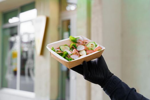Safety delivery with mask and black medical gloves at quarantine period. Salad in eco thermo box