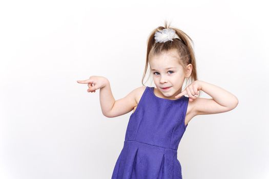 cute 5-6 year old girl in a blue dress posing in the studio. the child points to a place. banner for advertising