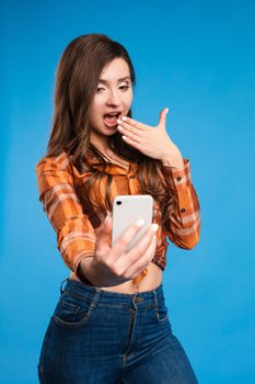 Full length portrait of happy stylish woman with charming smile in fashion sweater and brown skirt. She is standing and taking selfie with smartphone. Isolated on gray background