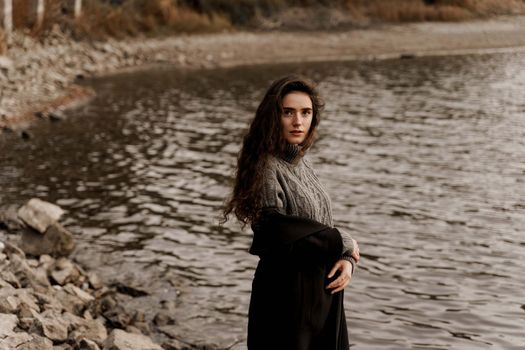 Young woman with curly hair looks at the lake and dreams about her life