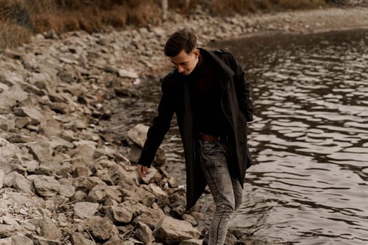 Confident male model weared black fashion coat. Handsome man walks near lake
