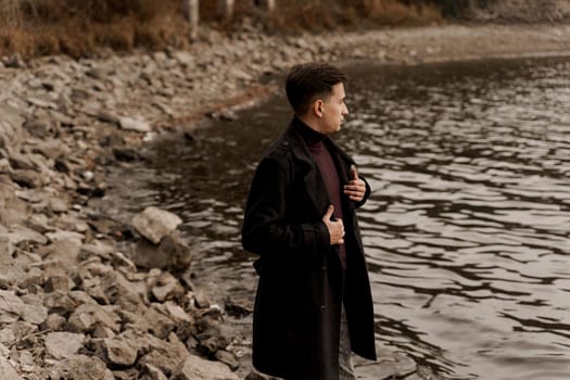 Confident business man walks near lake and thinks about his business during quarantine coronavirus covid-19 period. Handsome male weared formal black coat