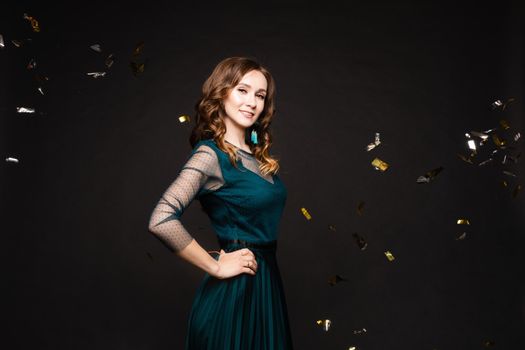 Front view of elegant woman wearing long black dress looking at camera and smiling on black isolated background. Attractive blonde with long legs posing in studio. Concept of party and beauty.