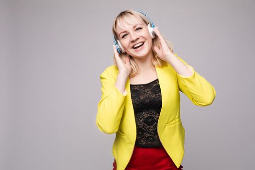 Front view of crazy curly woman with makeup wearing headphones and listening music on isolated background. Pretty girl dancing, singing and enjoying song in studio. Concept of disco and party.