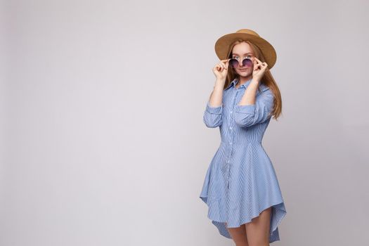 Front view of bright young girl wearing straw hat and glasses posing on isolated background in studio. Female tourist, looking at camera and smiling. Concept of summer.