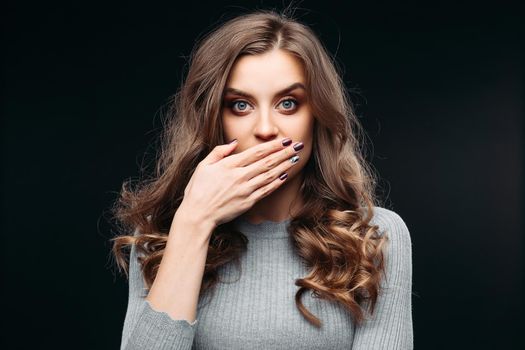 Waist up portrait of surprised beautiful girl with nice long hair, perfect makeup and fashion manicure. She is looking at camera with astonishment. Isolated on dark background