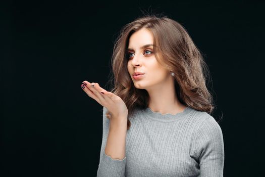 Portrait of charming girl with excellent fashion hairstyle and professional natural makeup. Sensual female looking away and sending air-kiss. Isolated on dark background