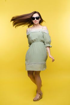 Full length portrait of a brunette woman in plain pale green dress and sandals and sunglasses turning around at camera. Captured in motion.