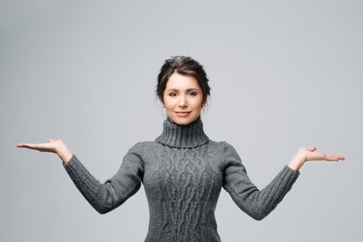 Waist up portrait of smiling woman presenting something, proposing making choice between two things or objects. Attractive brunette looking at camera with happiness. Isolated on gray background