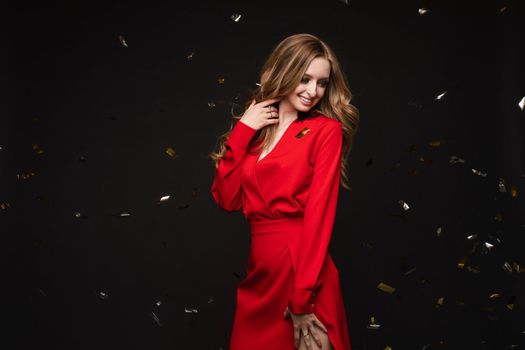 Front view of elegant woman wearing long black dress looking at camera and smiling on black isolated background. Attractive blonde with long legs posing in studio. Concept of party and beauty.