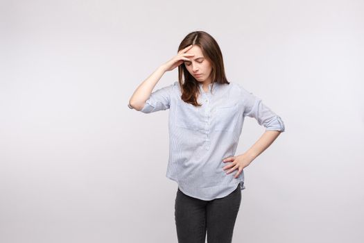 Studio portrait of attractive young brunette woman suffering from a bad migraine or headache. She is holding hand on her forehead in pain.